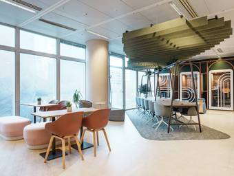 Espace de travail partagé, avec une grande table sous un plafond acoustique et des cabines téléphoniques