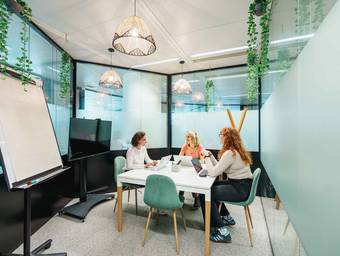 Trois femmes en réunion autour d'une table, dans une petite salle vitrée d'un espace de coworking
