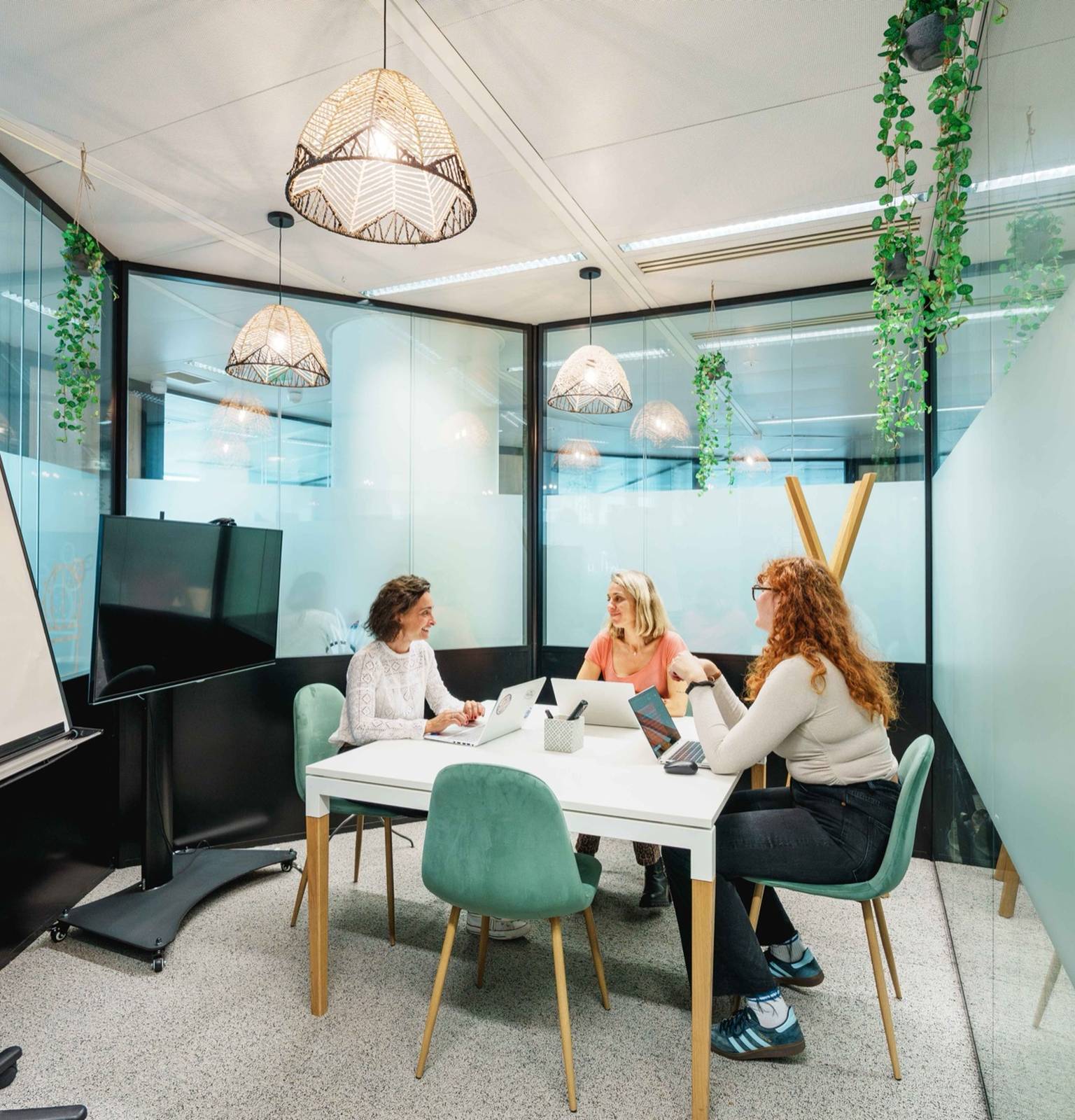 Trois femmes en réunion autour d'une table, dans une petite salle vitrée d'un espace de coworking